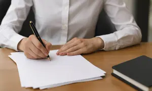 Main d'une personne écrivant sur du papier avec un stylo, à côté d'un carnet.