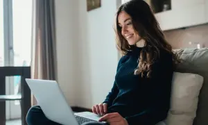 Jeune femme souriante travaillant sur son ordinateur portable, rédigeant sa lettre de motivation master MEEF.