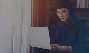 Jeune homme avec des écouteurs et des lunettes travaille sur son ordinateur portable, rédigeant une lettre de motivation intérim sans expérience.