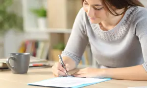 Femme écrivant une lettre de motivation sur un bureau avec une tasse de café.