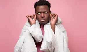 Homme frustré met des bouchons d'oreilles, enveloppé dans une couette. Il prépare sa lettre de nuisance sonore au maire.