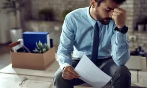 Homme stressé tenant une lettre de plainte au syndic de copropriété, avec une boîte de déménagement derrière lui.