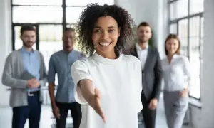 Une femme souriante tend la main, prête à aider pour une demande de local gratuit pour association. Son équipe est derrière elle.