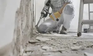 Un ouvrier utilise un marteau-piqueur pour démolir un mur. Des débris jonchent le sol. C'est une étape de travaux, comme dans une lettre d'information.