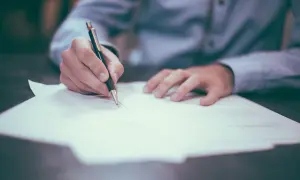 Main tenant une plume, écrit sur un document.