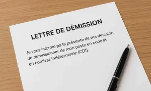 Une lettre de démission CDI avec préavis est posée sur un bureau en bois, avec un stylo noir à côté.