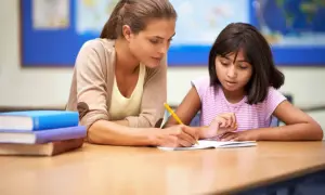 Une éducatrice aide une élève à écrire dans son cahier. Une scène qui pourrait figurer dans une lettre de motivation éducateur.