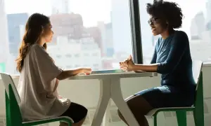 Deux femmes discutent à une table, l'une semble faire une demande d'entretien avec son directeur.