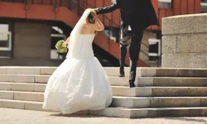 Un couple monte les marches, la mariée en robe blanche tenant un bouquet, le marié en costume noir. Une scène symbolisant leur union, peut-être après une lettre mariage mairie.