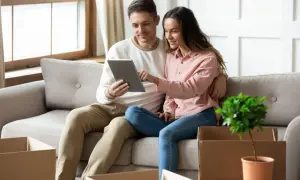 Couple sur un canapé, regardant une tablette. Des cartons de déménagement sont autour d'eux, peut-être pour une lettre pour quitter son logement sans préavis.