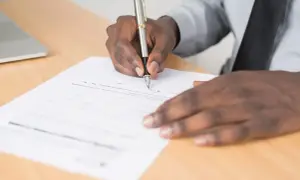 Main noire signant un document, peut-être une lettre de motivation pour un poste d'électrotechnicien.