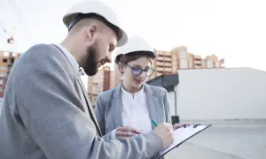 Deux ingénieurs, casques blancs, discutent d'un document sur un chantier. L'un signe, peut-être un modèle attestation employeur.