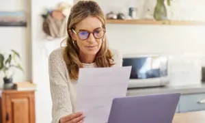 Femme concentrée sur un document, peut-être un modèle lettre déclaration tardive impôts, devant son ordinateur.