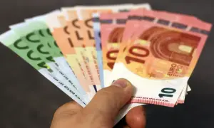 Main d'une personne tenant plusieurs billets en euros, dont des 10€ et 100€. Une scène évoquant une reclamation caisse epargne.