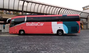 Un bus BlaBlaCar rouge et gris est garé sur une place pavée sous un auvent.