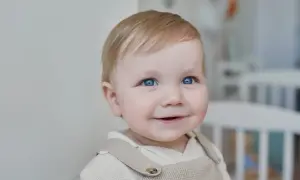 Un bébé aux yeux bleus pétillants sourit, prêt pour sa lettre demande de place en crèche urgent.