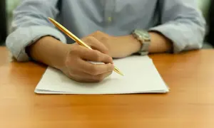 Main tenant une plume dorée, une personne rédige une lettre de motivation STAPS sur une feuille blanche.