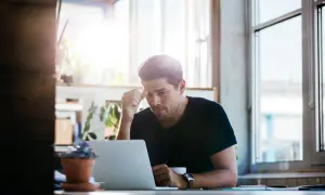 Un homme pensif devant son ordinateur, rédigeant un mail relance entretien. La lumière du jour éclaire son visage concentré.