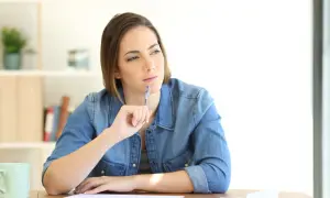 Femme songeant à une lettre de remise gracieuse impot taxe d'habitation, stylo à la main, devant des papiers.