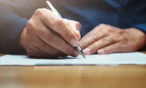 Main tenant rédigeant une lettre, peut-être un modèle lettre CARSAT, avec un stylo argenté sur un document.
