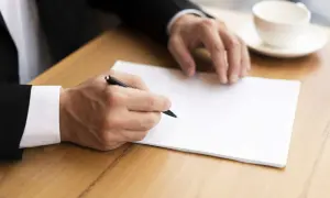 Homme en costume écrivant une lettre. Il pourrait s'agir d'une démarche concernant le harcèlement moral, avec l'aide de la médecine du travail.