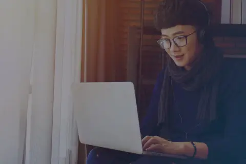 Jeune homme avec des écouteurs et des lunettes travaille sur son ordinateur portable, rédigeant une lettre de motivation intérim sans expérience.