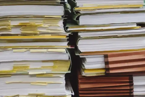 Piles of documents, some with yellow tabs, suggest a complex administrative process, perhaps a demande de relevé de carrière par courrier.