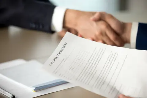 Poignée de main après la signature d'un contrat. Une lettre de motivation pour un poste d'assistant manager est visible.