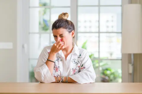 Femme pince son nez, visiblement incommodée par des nuisances olfactives. Elle prépare peut-être une lettre au maire.