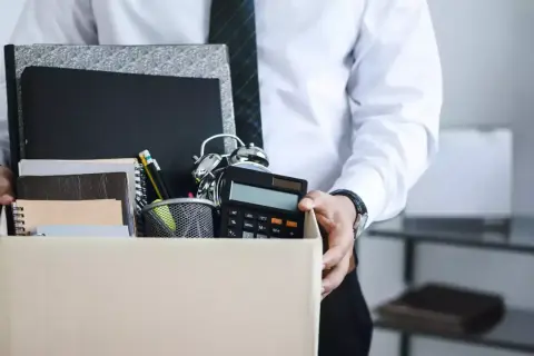Un étudiant quitte son emploi, portant une boîte remplie d'objets de bureau, symbolisant une lettre de démission contrat étudiant sans préavis.