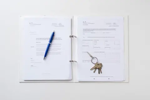 Un classeur blanc ouvert sur des documents. Un stylo bleu repose sur la page de gauche, tandis qu'un trousseau de clés est posé sur la page de droite, suggérant une lettre de demande de mutation ou un contrat.