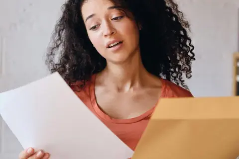 Jeune femme perplexe devant sa lettre de motivation Parcoursup. Elle tient un document blanc et une enveloppe marron.