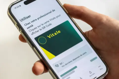 Main d'une personne tenant un smartphone affichant la carte Vitale numérique. Idéal pour le courrier restitution carte vitale.