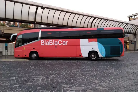 Un bus BlaBlaCar rouge et gris est garé sur une place pavée sous un auvent.