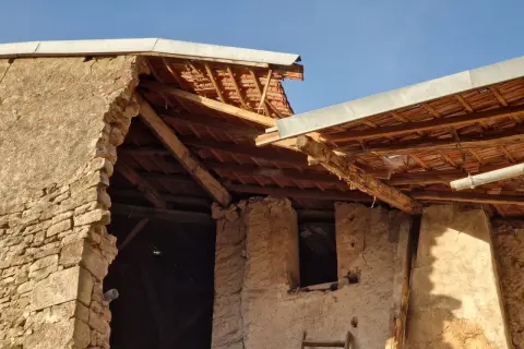 Mise en demeure : mur écroulé du voisin. Bâtiment en ruine, toiture endommagée, ciel bleu.