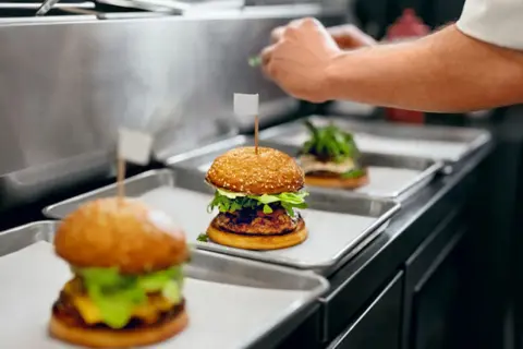 Trois hamburgers appétissants sur des plateaux, prêts pour la livraison. Une image parfaite pour une lettre de motivation restauration rapide.