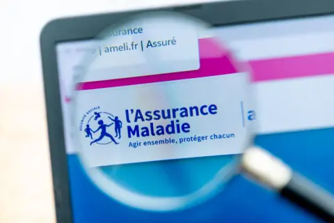 Loupe sur l'écran d'un ordinateur affichant le site ameli.fr, logo de l'Assurance Maladie. Une lettre demande d'ouverture des droits à l'assurance maladie est en cours de consultation.