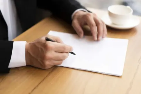 Homme en costume écrivant une lettre. Il pourrait s'agir d'une démarche concernant le harcèlement moral, avec l'aide de la médecine du travail.