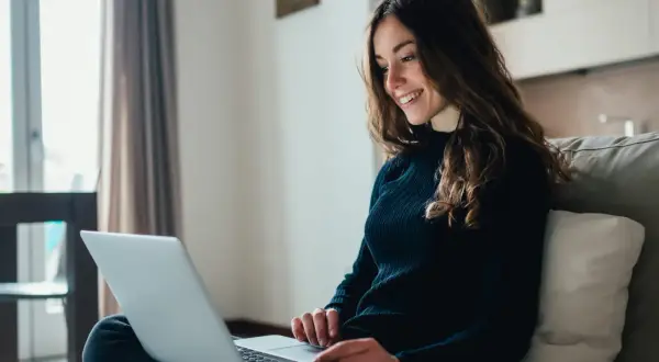 Jeune femme souriante travaillant sur son ordinateur portable, rédigeant sa lettre de motivation master MEEF.