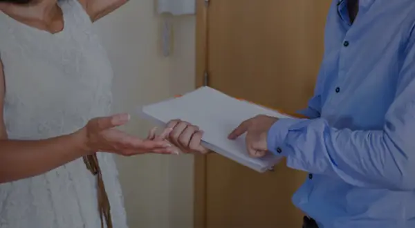Une femme en robe blanche reçoit des documents d'un homme en chemise bleue.