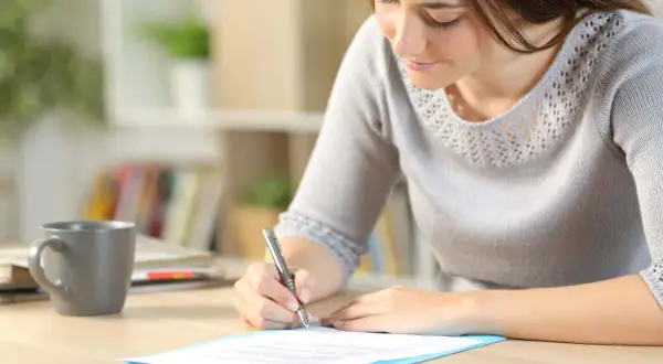 Femme écrivant une lettre de motivation sur un bureau avec une tasse de café.