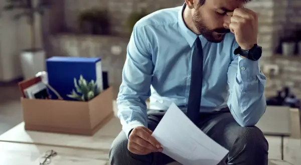 Homme stressé tenant une lettre de plainte au syndic de copropriété, avec une boîte de déménagement derrière lui.