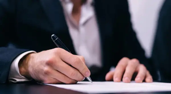Un homme en costume signe un document, peut-être un modèle lettre demande d'exonération.