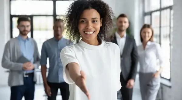 Une femme souriante tend la main, prête à aider pour une demande de local gratuit pour association. Son équipe est derrière elle.