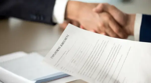 Poignée de main après la signature d'un contrat. Une lettre de motivation pour un poste d'assistant manager est visible.
