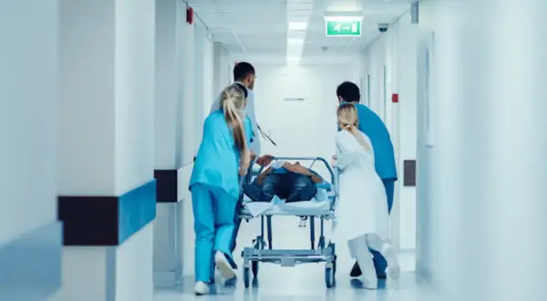 Équipe médicale transportant un patient sur un brancard dans un couloir d'hôpital. Idéal pour une lettre de motivation brancardier sans expérience.