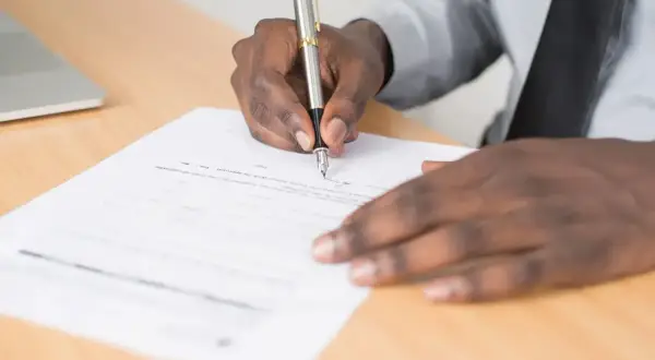 Main noire signant un document, peut-être une lettre de motivation pour un poste d'électrotechnicien.