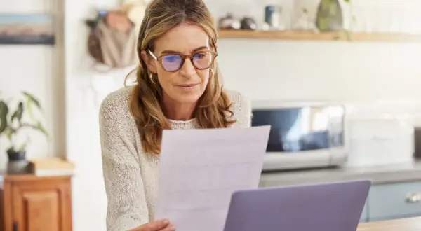 Femme concentrée sur un document, peut-être un modèle lettre déclaration tardive impôts, devant son ordinateur.