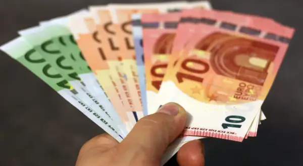 Main d'une personne tenant plusieurs billets en euros, dont des 10€ et 100€. Une scène évoquant une reclamation caisse epargne.
