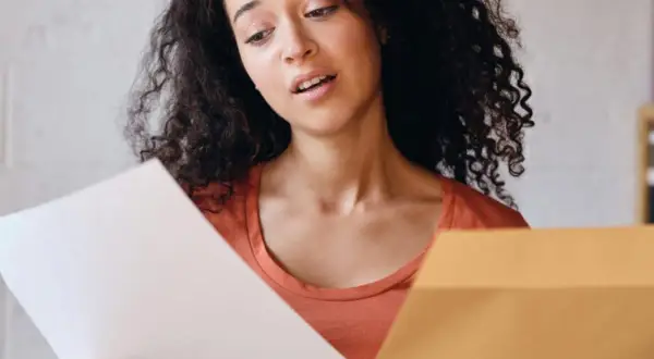 Jeune femme perplexe devant sa lettre de motivation Parcoursup. Elle tient un document blanc et une enveloppe marron.